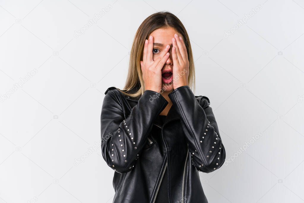 Young caucasian woman wearing a black leather jacket blink through fingers frightened and nervous.