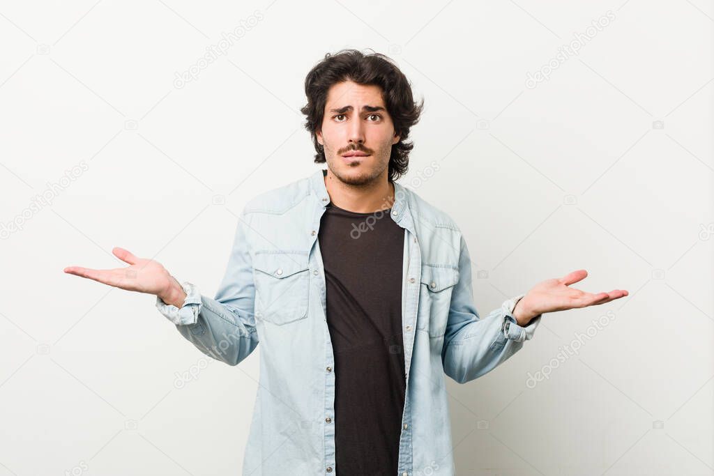 Young handsome man against a white background confused and doubtful shrugging shoulders to hold a copy space.