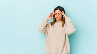 Mavi arka planda izole edilmiş genç bir kadın şakaklara dokunuyor ve başı ağrıyor..