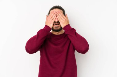 Beyaz bir arka planda izole edilmiş genç, uzun saçlı bir adam elleriyle gözlerini kapatıyor, geniş bir gülümsemeyle bir sürpriz bekliyor..