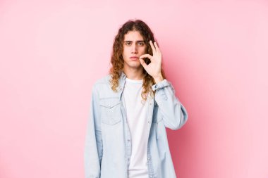 Uzun saçlı adam, izole bir şekilde poz veriyor. Parmakları dudaklarında, sır saklıyor..