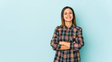 Mavi arka planda izole edilmiş, kendinden emin, kararlılıkla kollarını kavuşturan genç bir kadın..