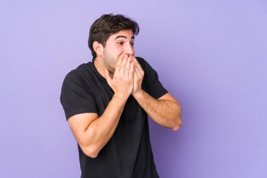 Mor arka planda izole olmuş genç bir adam bir şeye gülüyor, elleriyle ağzını kapatıyor..