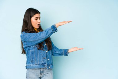 Mavi arka planda izole edilmiş genç Hintli kadın elleri arasında bir kopya alanı tutarken şok ve hayrete düştü..