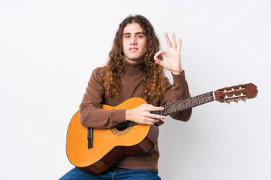 Gitar çalan beyaz bir adam neşeli ve kendinden emin bir şekilde iyi bir jest yapıyor..