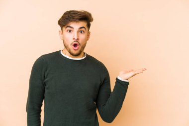 Bej bir arkaplanda izole edilmiş genç bir Arap, avuç içi fotokopi alanını tutmaktan etkilenmiş..