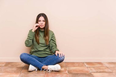 Genç, beyaz bir kadın yerde tek başına oturuyor. Parmakları dudaklarında, bir sırrı saklıyor..