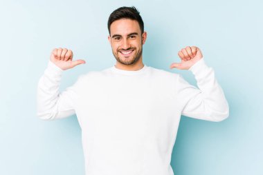 Mavi arka planda izole edilmiş genç beyaz adam gururlu ve kendinden emin hissediyor, örnek olarak.