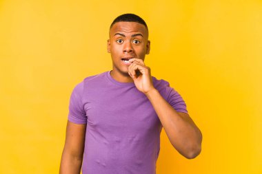 Sarı arka planda izole edilmiş, tırnak yiyen, gergin ve endişeli genç bir Latin..