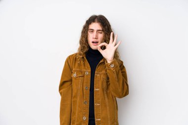 Uzun saçlı adam yalnız poz veriyor bir göz kırpıyor ve elleriyle iyi bir jest yapıyor..