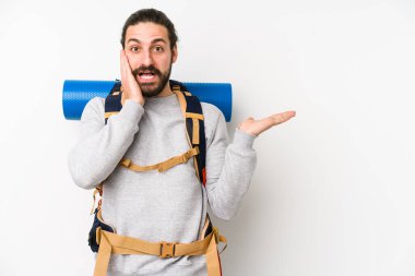 Beyaz arka planda izole edilmiş genç bir sırt çantalı adam avuç içinde fotokopi alanı tutuyor, el üstünde tutuyor. Şaşırmış ve mutlu..