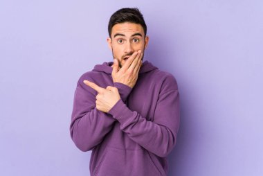 Mor arka planda izole edilmiş genç beyaz adam yan tarafı işaret ediyor.
