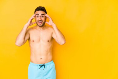 Sarı arka planda mayosu olan genç beyaz bir adam. Hoş bir sürpriz yapan, heyecanlı ve el kaldıran beyaz bir adam..