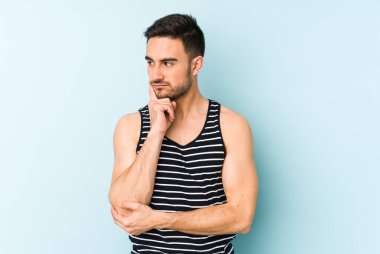 Kafkasyalı genç bir adam mavi arka planda izole edilmiş. Bir strateji planlıyor, bir iş yolu düşünüyor..