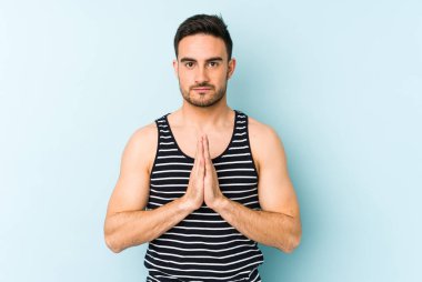 Kafkasyalı genç adam mavi arka planda izole edilmiş dua ediyor, bağlılık gösteriyor, dindar biri ilahi ilham arıyor..