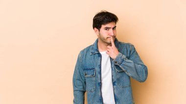 Genç adam bej arka planda izole edilmiş düşünüyor, bakıyor, yansıtıyor, düşünüyor, bir fantezi kuruyor..