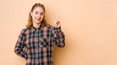 Beyaz tenli genç bir kadın bej arka planda izole edilmiş. Parmaklarıyla taş hareketi gösteriyor.