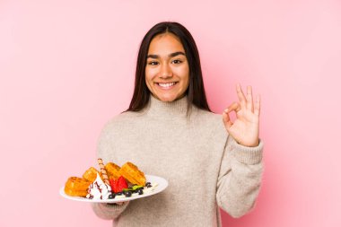 Elinde waffle tutan genç Asyalı kadın neşeli ve kendinden emin, iyi bir jest yapıyor..