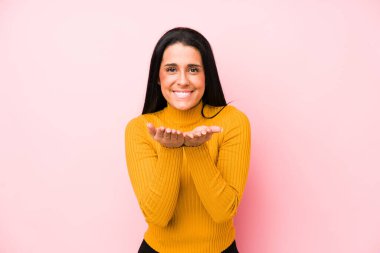 Pembe arka planda izole edilmiş beyaz bir kadın elinde avuç içi bir şeyle kameraya sunuyor..