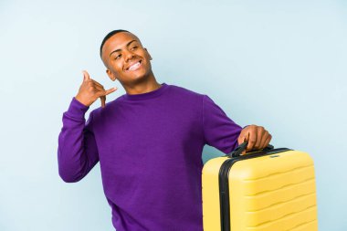 Elinde bavul tutan genç bir gezgin parmaklarıyla bir cep telefonu hareketi gösteriyor..