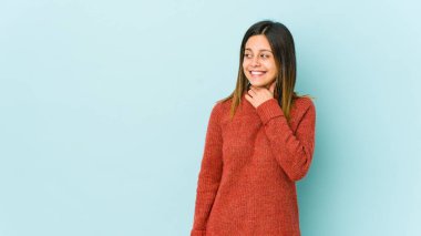 Mavi arka planda izole edilmiş genç bir kadın kafasının arkasına dokunuyor, düşünüyor ve bir seçim yapıyor..