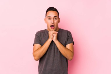 Pembe arka planda poz veren Latin adam şans için dua ediyor, şaşırıyor ve ağzını açıyor..