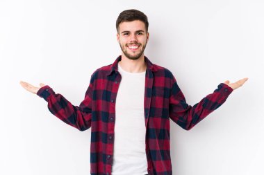 Beyaz arka planda poz veren beyaz tenli genç adam kollarıyla ölçek oluşturuyor, mutlu ve kendinden emin hissediyor..