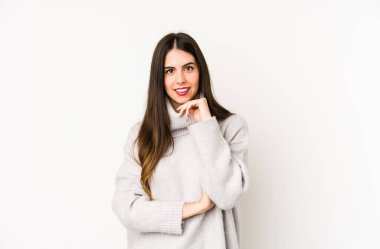 Beyaz bir arka planda izole edilmiş genç beyaz kadın mutlu ve kendinden emin gülümsüyor, elleriyle çenesine dokunuyor..