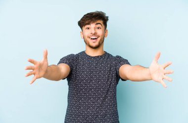 Mavi arka planda izole edilmiş genç bir Arap adam kameraya sarıldığı için kendinden emin hissediyor..