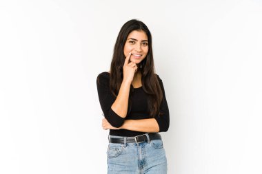 Mor arka planda izole edilmiş genç Hintli kadın mutlu ve kendinden emin gülümsüyor, elleriyle çenesine dokunuyor..