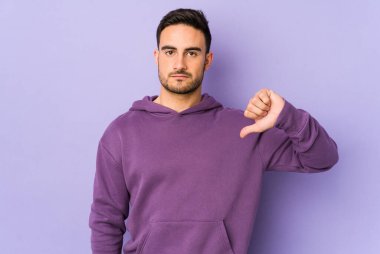 Mor arka planda izole edilmiş genç beyaz bir adam hoş olmayan bir jest yapıyor, başparmakları aşağıda. Anlaşmazlık konsepti.