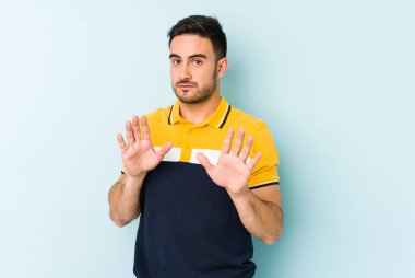 Mavi arka planda izole edilmiş genç beyaz adam tiksinti belirtisi gösteren birini reddediyor..