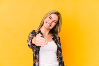 Sarışın, beyaz bir kadın sarı arka planda izole edilmiş. Kameraya doğru elini uzatarak selam veriyor..