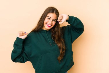 Beyazlı genç bir kadın bej arka planda izole edilmiş özel bir günü kutluyor, atlıyor ve enerji ile kollarını kaldırıyor..