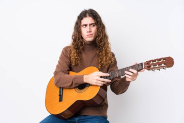 Gitar çalan beyaz bir adam kafası karışmış, kendinden emin değil..