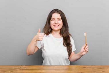 Elinde diş fırçası tutan, gülümseyen ve baş parmağını kaldıran bir kadın.