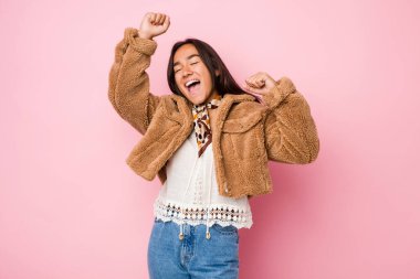 Özel bir günü kutlamak için kısa bir koyun derisi ceket giyen genç Hintli kadın atlıyor ve enerjiyle kollarını kaldırıyor..