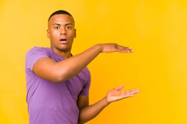 Sarı arka planda izole edilmiş genç Latin adam elleri arasında bir kopya alanı tutarken şok ve hayrete düştü..