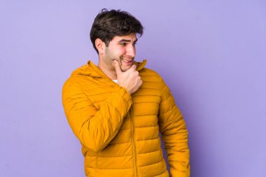 Mor arka planda izole edilmiş genç bir adam kafasının arkasına dokunuyor, düşünüyor ve bir seçim yapıyor..