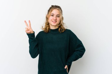 Beyaz arka plandaki genç beyaz kadın iki numarayı parmaklarıyla gösteriyor..