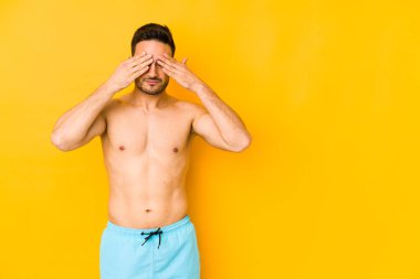 Sarı arka planda mayosu olan genç, beyaz bir adam. Kafası ağrıyan, yüzüne dokunan beyaz bir adam..