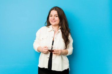 Genç kavisli kadın elinde çay bardağıyla mutlu, güler yüzlü ve neşeli.