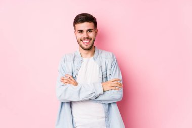 Beyaz arka planda poz veren beyaz tenli genç bir iş adamı kendinden emin ve kararlı bir şekilde kollarını kavuşturuyor..