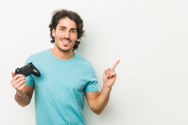 Oyun kumandası tutan genç adam işaret parmağıyla işaret ederek gülümsüyor..