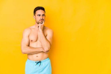 Sarı arka planda yalıtılmış beyaz mayo giyen genç, beyaz tenli bir adam. Düşünüyor, bakıyor, yansıtıyor, düşünüyor, bir fantezi kuruyor..