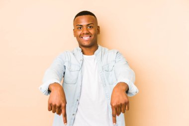 Bej arka planda izole edilmiş genç latin adam parmakları aşağıda, pozitif duygu..