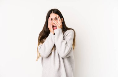 Beyaz arka planda izole edilmiş beyaz tenli genç bir kadın korkmuş ve gergin parmaklarıyla göz kırpıyor..