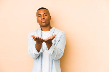 Genç latin adam bej arka planda izole edilmiş dudaklar kıvrılmış ve hava öpücüğü göndermek için avuç içleri tutulmuş..