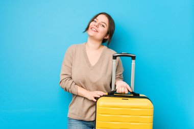 Genç kavisli kadın elinde bavulla gülüyor ve eğleniyor..