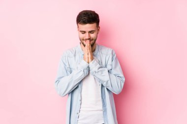 Beyaz arka planda poz veren beyaz tenli genç bir iş adamı yalnız başına el ele dua ederken, kendine güveniyor..